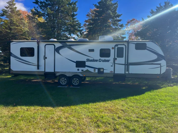White Shadow Cruiser RV rental on grass, surrounded by trees under a blue sky. Ready for your next outdoor trip!. Cruiser RV Shadow Cruiser 2015