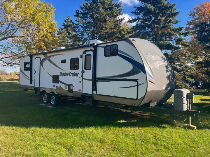 White Shadow Cruiser RV rental: a modern travel trailer parked on green grass with extended slide-out, surrounded by trees.. Cruiser RV Shadow Cruiser 2015
