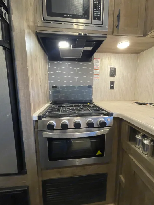 Inside an RV rental: a compact kitchen with a stainless steel stove, oven, microwave, and sleek grey tile backsplash.. Palomino Puma 2021