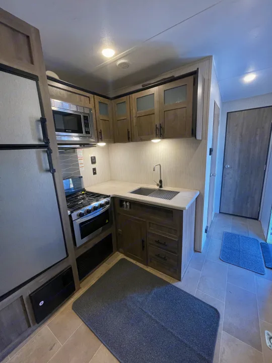 Well-equipped RV rental kitchen with stainless steel microwave, stove, sink, fridge, wood cabinets, and tiled floor.. Palomino Puma 2021