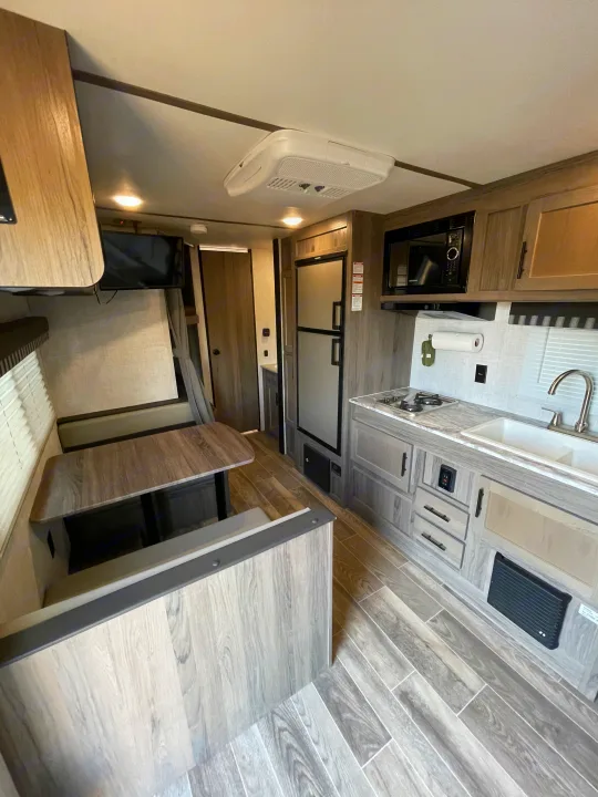 Modern RV rental interior: well-equipped kitchen with fridge, stove, sink, plus a comfy dinette & wall-mounted TV.. Gulf Stream Enlighten 2021