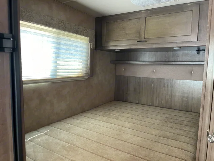 This cozy RV rental bedroom features a comfortable bed, a bright window with blinds, and practical overhead cabinets.. Winnebago Minnie Winnie 2019