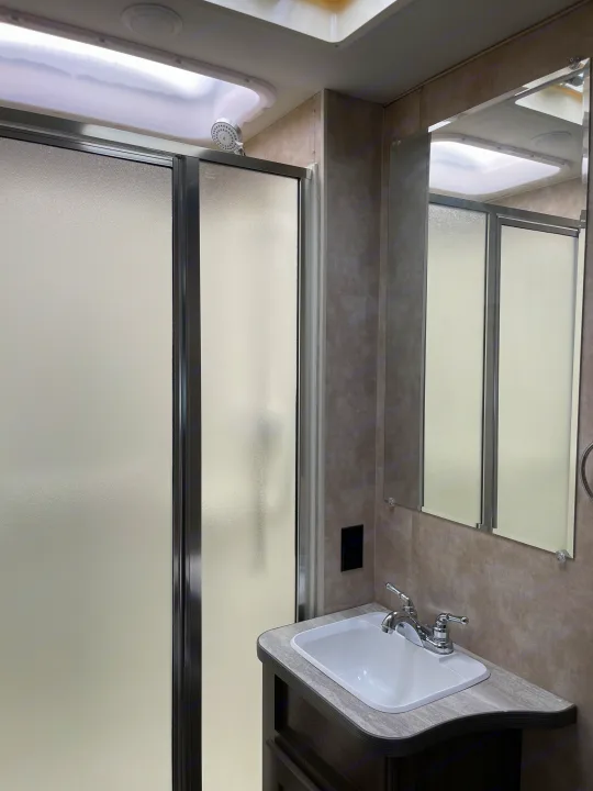 Modern RV rental bathroom featuring a frosted glass shower, integrated lighting, vanity with sink, and mirror.. Winnebago Minnie Winnie 2019