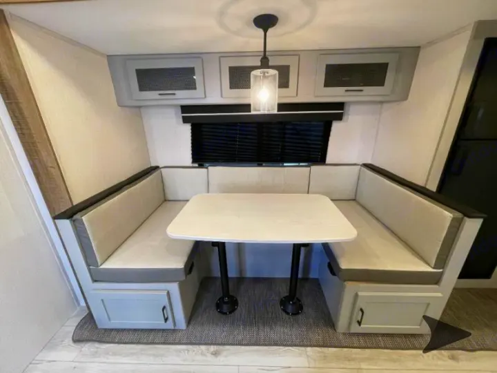 Modern RV rental dinette featuring U-shaped bench seating, a central table, and overhead cabinets for storage.. Heartland RVs North Trail 2024