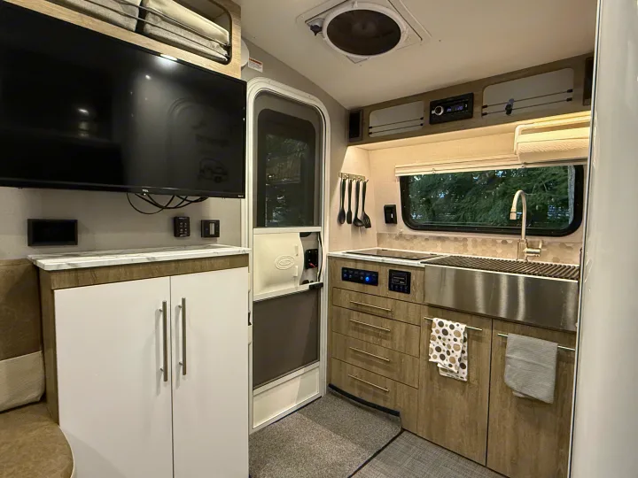 Modern RV rental interior showing a full kitchen with sink, cooktop, cabinets, and TV viewing area. Ideal for travel.. InTech RV SOL 2021