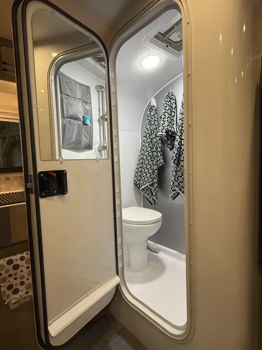 This RV rental shows a compact, light gray wet bath with white toilet, shower, and black/white patterned towels.. InTech RV SOL 2021