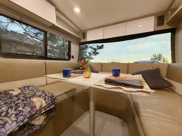 Cozy RV rental dining area with a marble table, two mugs, flowers, and comfy benches, illuminated by natural light.. InTech RV SOL 2021