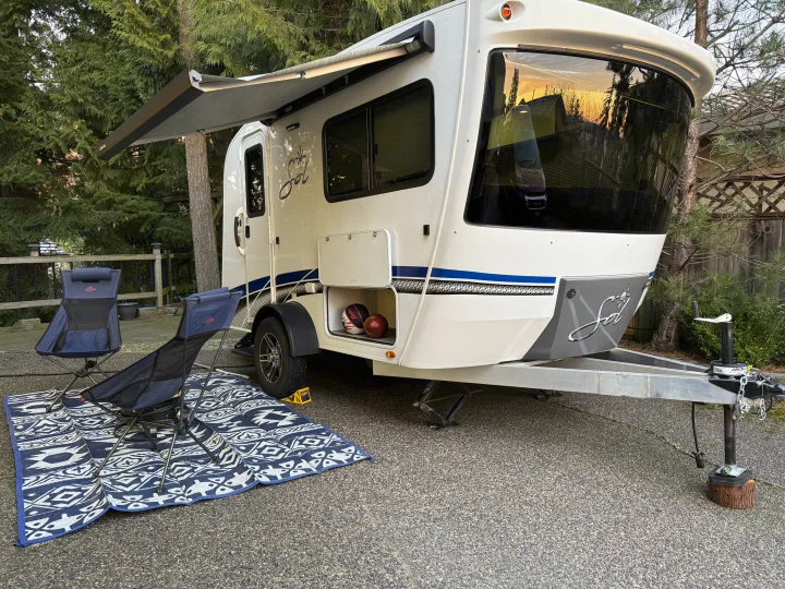Cozy RV rental setup: white travel trailer with extended awning, camping chairs, and outdoor mat for ultimate leisure.. InTech RV SOL 2021