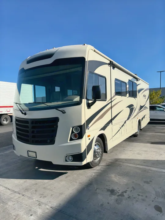 Spacious, cream-colored Class A motorhome RV rental, adorned with black and brown graphics, parked on a sunny lot.. FR3 FR3 Motorhome 2018