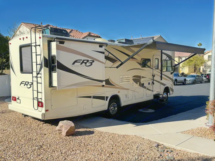 Beige FR3 RV rental: a spacious motorhome with slides extended and awning out, parked on gravel in sunlight.. FR3 FR3 Motorhome 2018