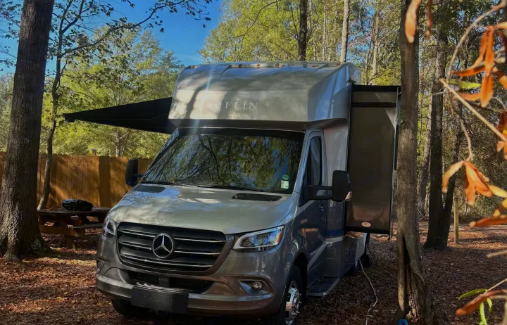 This Tiffin Mercedes-Benz RV rental is parked with its awning and slide-out extended in a serene, wooded campsite.. Wayfarer Wayfarer Motorhome 2021