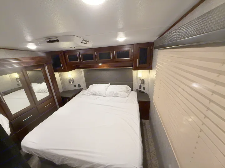 Comfortable RV rental bedroom showcasing a cozy bed, dark wood cabinets, and an overhead AC unit.. Forest River Vengeance Toy Hauler 2019