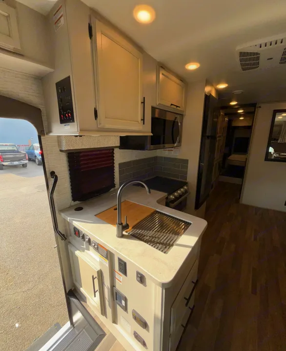 Inside a bright RV rental: kitchen counter with sink & stove, microwave, cabinets, and wood flooring leading to the bedroom area.. Entegra Odyssey 30Z 2024