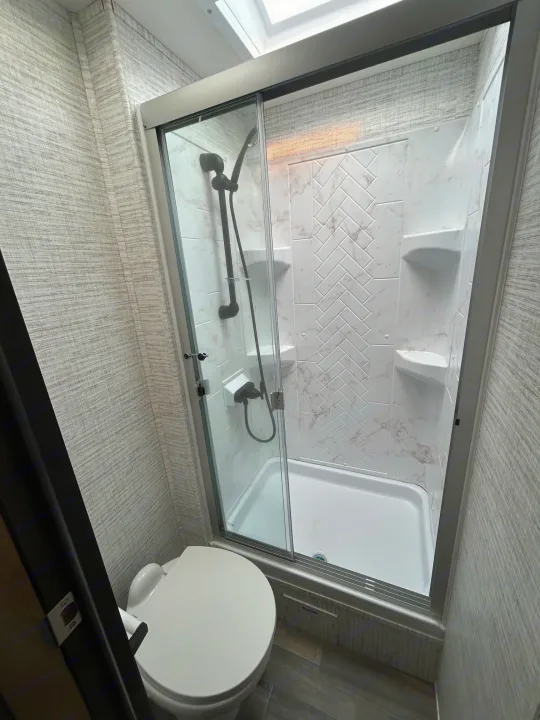 RV rental bathroom interior with a white toilet and modern glass-enclosed shower, featuring marble-look walls.. Entegra Odyssey 30Z 2024