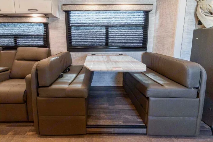 Modern RV rental dinette featuring comfy booth seating, a table with cupholders, and large windows with blinds.. Entegra Odyssey 30Z 2024