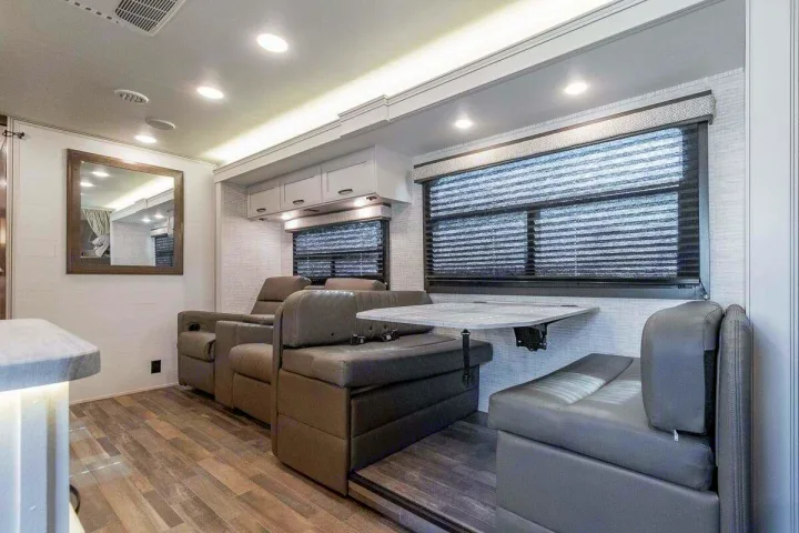 Modern RV rental interior showing a bright living and dining area with gray recliners and a convertible dinette.. Entegra Odyssey 30Z 2024