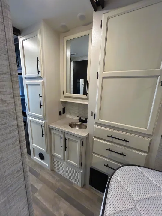 This RV rental interior features a bedroom area with ample storage cabinets, a vanity with a sink, and a comfortable bed.. Entegra Odyssey 30Z 2024