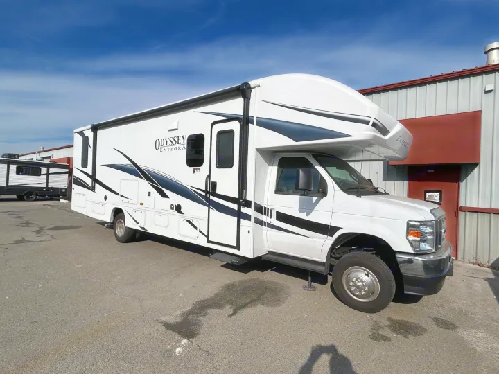 Bright white Odyssey Entegra Class C RV rental parked on an asphalt lot under a blue sky.. Entegra Odyssey 30Z 2024
