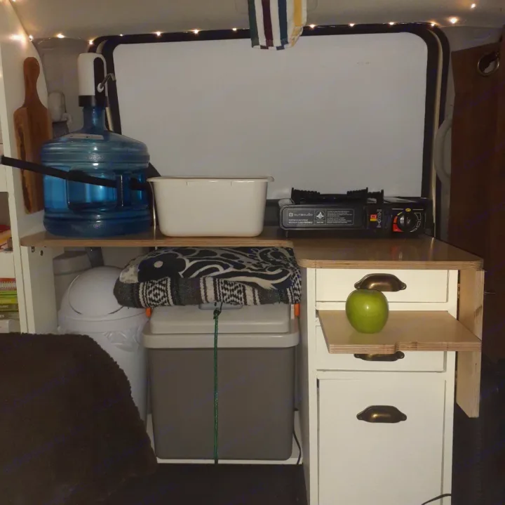 Compact kitchen in an RV rental: water dispenser, stove, cooler, and storage for mobile living.. Dodge 24ft 2010