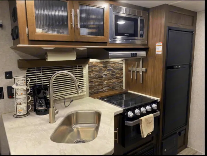 Compact RV rental kitchen: sink, stove, microwave, and fridge, designed for comfortable travel cooking.. Forest River Cherokee Grey Wolf 2019