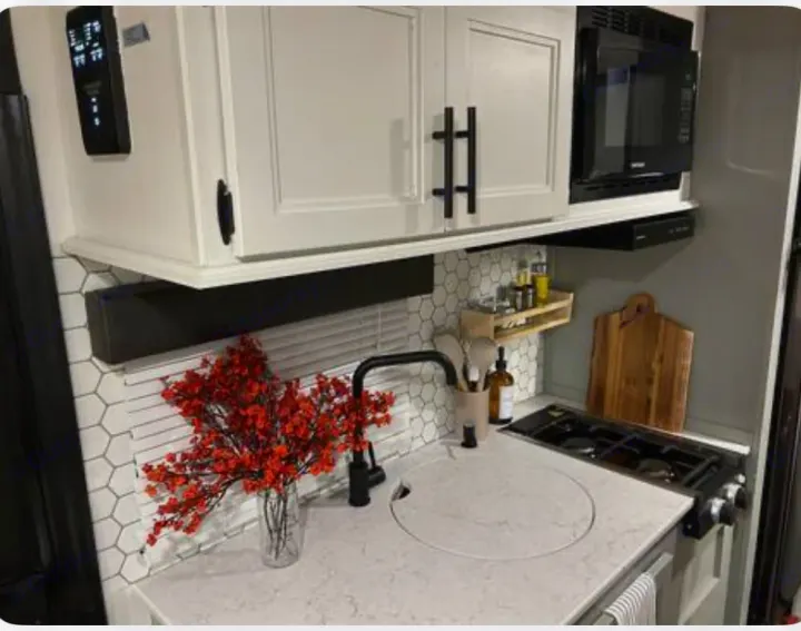 Modern RV rental kitchen with white cabinets, microwave, stovetop, and sink. A vase of red flowers adds color.. Forest River Cherokee Wolf Pup 2022