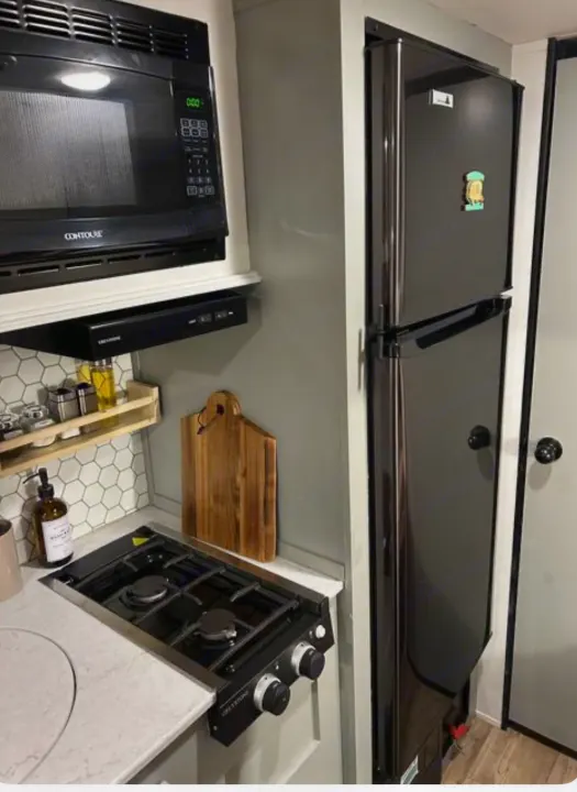 Compact RV rental kitchen with a black microwave, range hood, two-burner stove, and tall black refrigerator, ideal for travel.. Forest River Cherokee Wolf Pup 2022