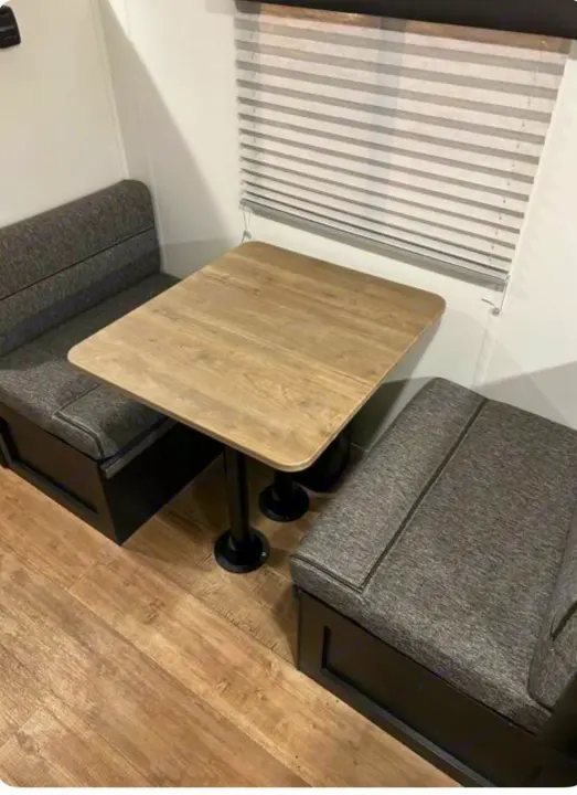 Cozy RV rental dinette featuring a light wood table, dark gray upholstered bench seating, and window blinds.. Forest River Cherokee Wolf Pup 2022