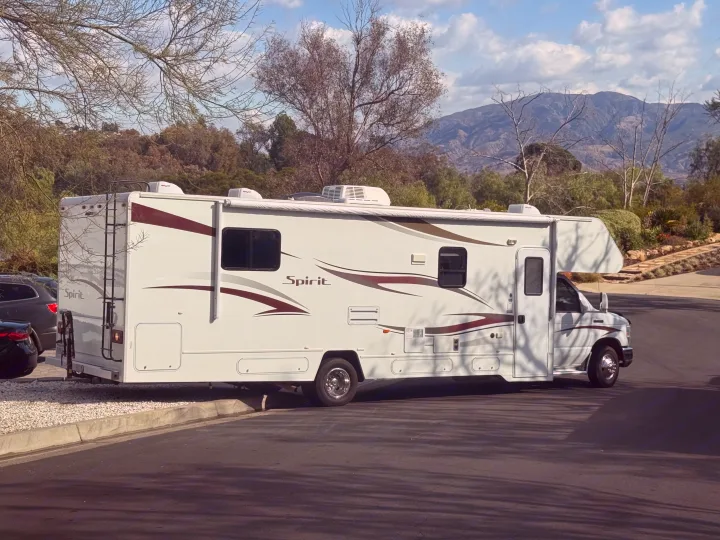 White Spirit RV rental parked on a street with mountains and trees in background, perfect for outdoor travel & recreation.. Itasca Spirit 2014