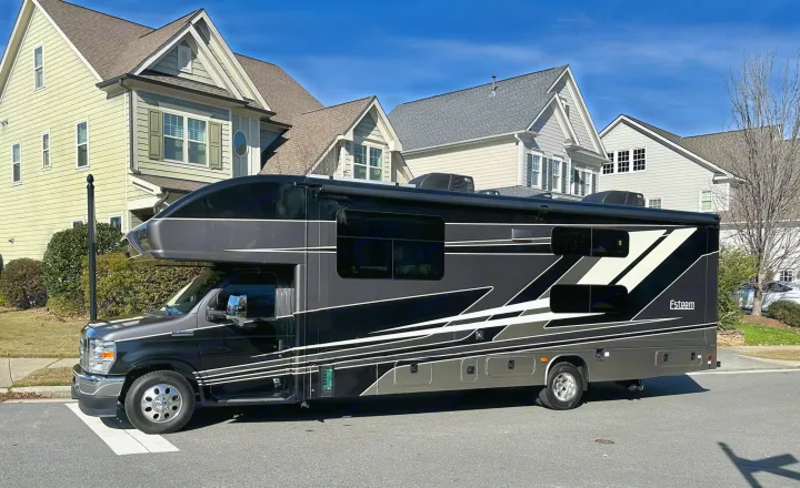 This modern dark gray and black Esteem Class C motorhome, an ideal RV rental, is parked on a sunny street.. Entegra Coach Esteem 2023