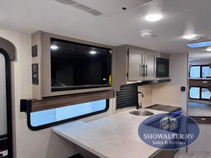 RV rental interior: modern kitchen, mounted TV, and glimpse of bunk beds for travel comfort.. K-Z Manufacturing Connect Mini 231BH 2025