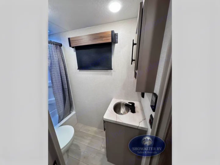 RV rental bathroom features a compact shower with patterned curtain, toilet, and vanity sink.. K-Z Manufacturing Connect Mini 231BH 2025