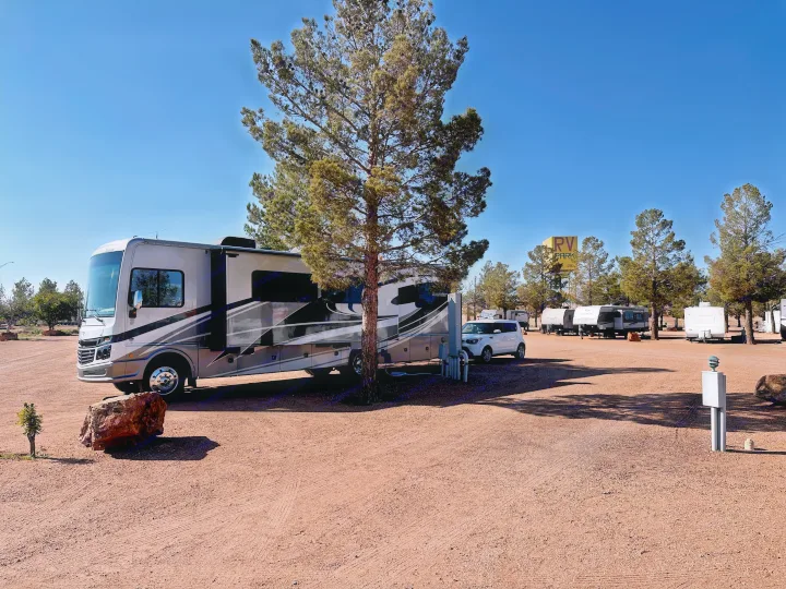 An RV rental motorhome is parked at a spacious RV park campsite under a clear blue sky, surrounded by trees and other RVs.. Fleetwood Bounder 33C 2021