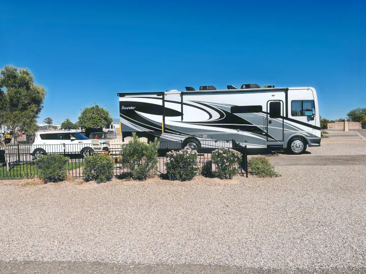 A large, black and white Bounder RV rental is parked on a gravel site under a clear blue sky, with a white car in the background.. Fleetwood Bounder 33C 2021