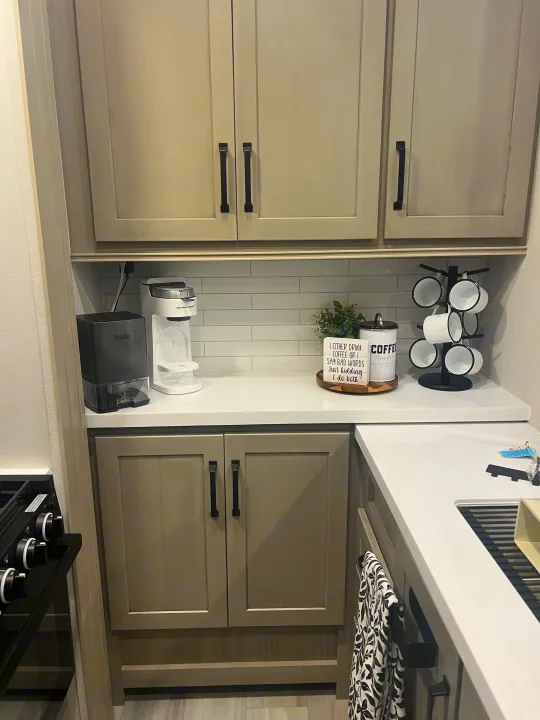 Enjoy a convenient coffee station in this modern RV rental kitchen, featuring sleek cabinets and white counters.. Grand Design Momentum 2025