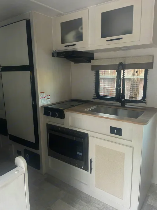 Bright and modern RV rental kitchen featuring a large fridge, stovetop, microwave, and sink with light cabinetry.. No Boundaries NoBo 19.3 Essentials Only 2024