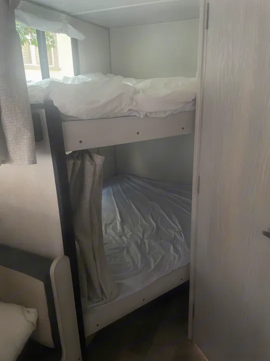 An RV rental bedroom featuring bunk beds; the top bunk enjoys window views, while the lower offers privacy with a curtain.. No Boundaries NoBo 19.3 Essentials Only 2024