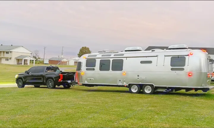 Black pickup truck towing a polished Airstream travel trailer on grass, an ideal RV rental for your next adventure.. Airstream International 2022