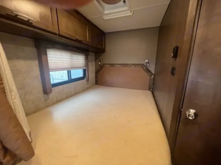 View inside an RV rental bedroom with a light-colored mattress, overhead wood cabinets, and a window.. Adventurer Adventurer Motorhome 2017