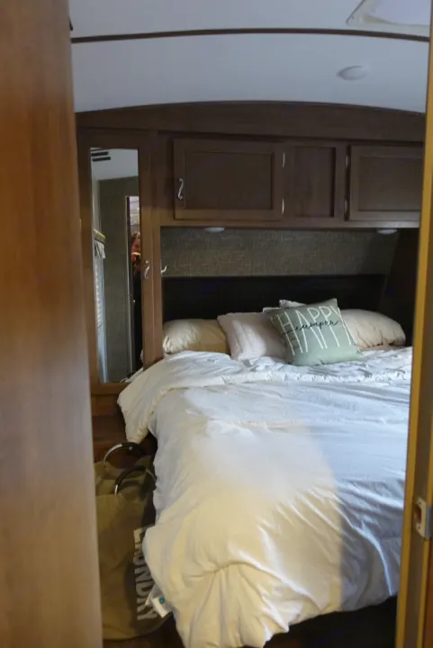 Cozy RV rental bedroom with comfortable bed, white bedding, and a "Happy Camper" pillow.. KZ Spree 2017