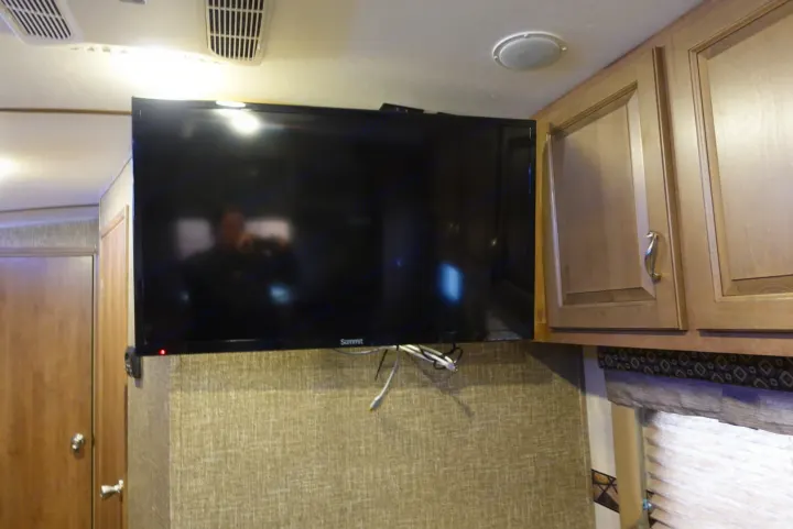 An RV rental interior featuring a large wall-mounted TV, light wood cabinets, and ceiling vents.. KZ Spree 2017