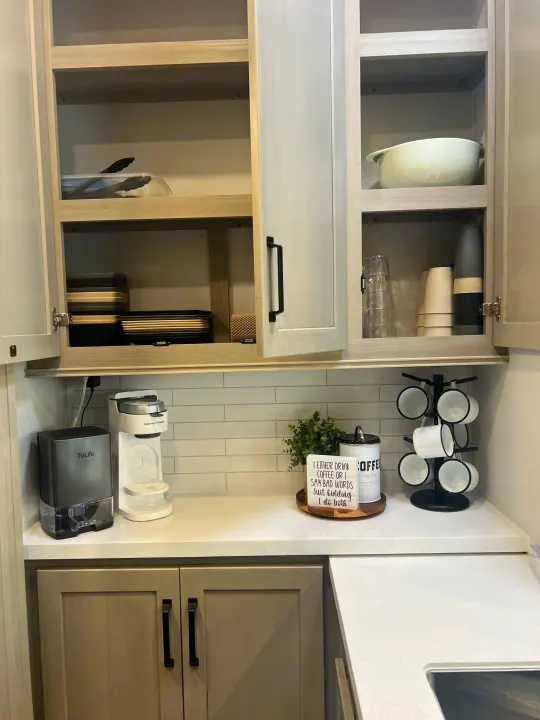 Well-organized RV rental kitchen with open cabinets showing dishes, glasses, and a coffee station on the counter, including mugs.. Grand Design Momentum 2025