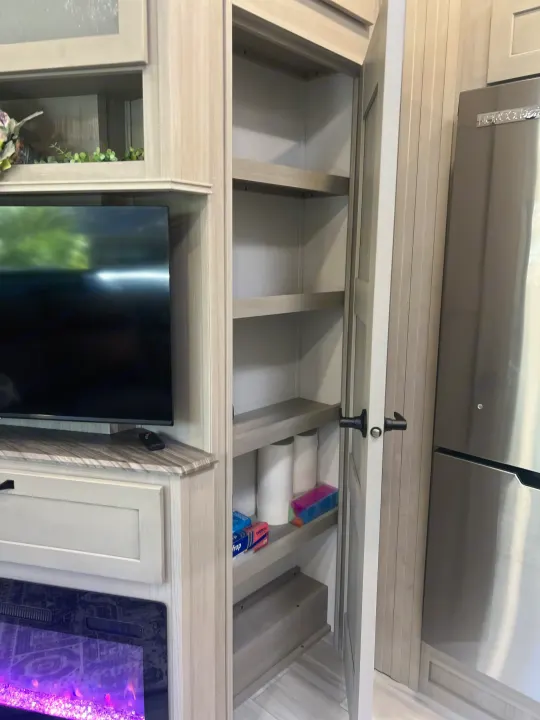 RV rental interior: TV, electric fireplace, and a well-organized pantry adjacent to the fridge. Ample storage for your trip.. Grand Design Momentum 2025