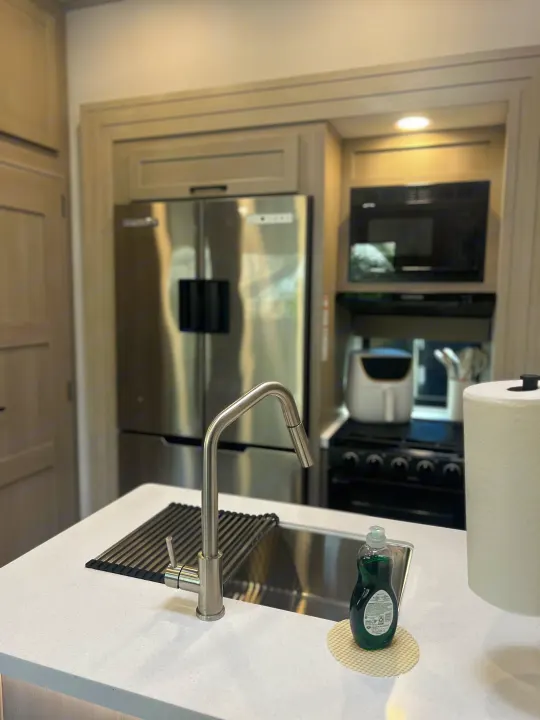 Enjoy a functional RV rental kitchen: stainless steel fridge, microwave, stove, sink with faucet, dish soap, & paper towels.. Grand Design Momentum 2025