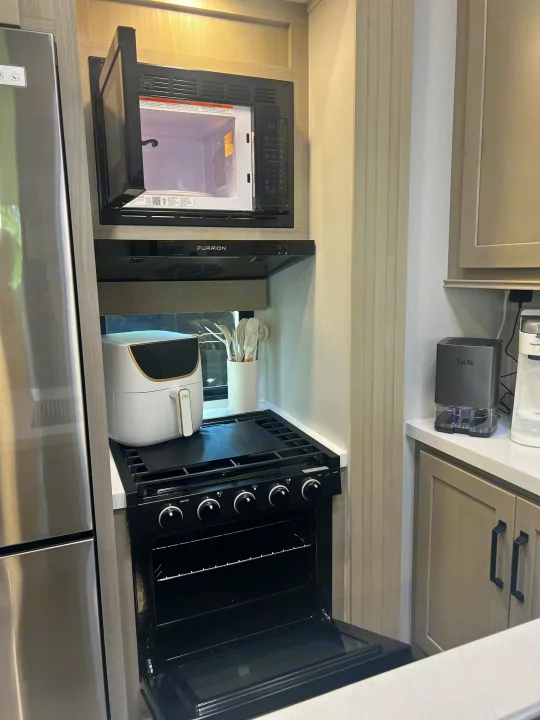 RV rental kitchen showing a stainless fridge, open microwave & oven, air fryer, and stove. All essentials.. Grand Design Momentum 2025