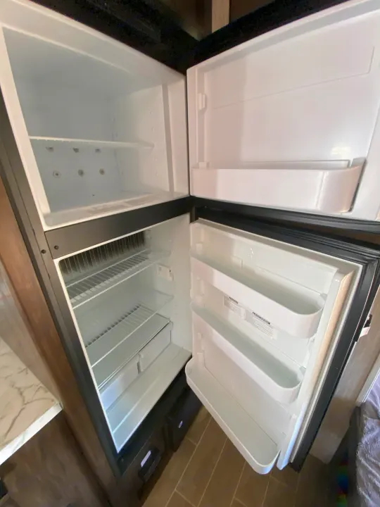 Open RV rental refrigerator: spacious, clean interior with empty shelves and door bins, ready for your trip.. Forest River Cherokee Wolf Pup 2020