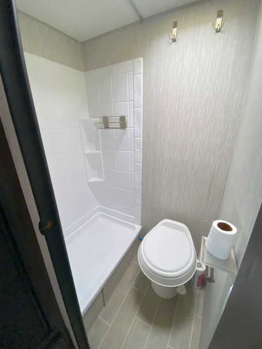 Clean RV rental bathroom with a compact shower stall on the left and a toilet on the right, featuring hooks and toilet paper holder.. Forest River Cherokee Wolf Pup 2020
