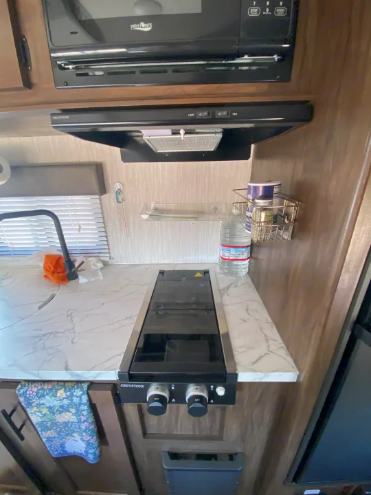 RV rental kitchen: a compact space featuring a 2-burner Greystone cooktop, High Pointe microwave, and countertop.. Forest River Cherokee Wolf Pup 2020