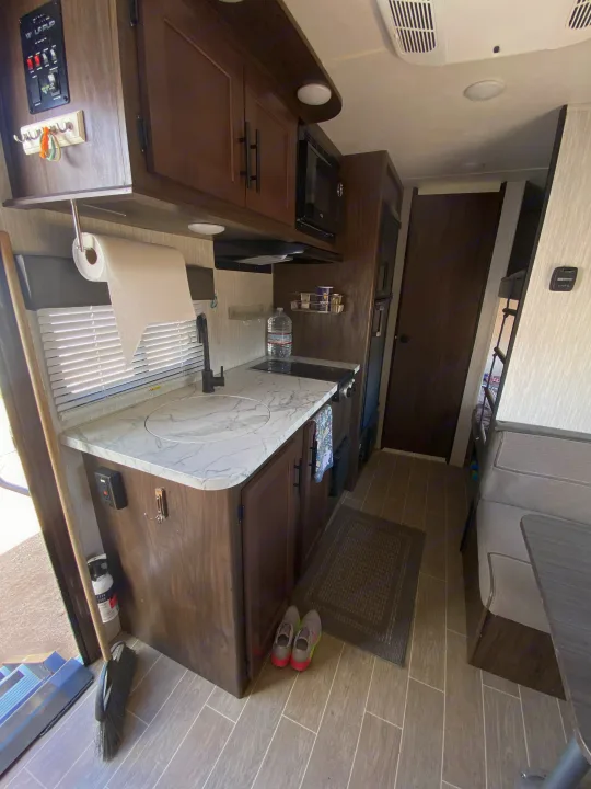 Modern RV rental interior: well-equipped kitchen with marble-look counters, dark cabinets, and nearby dining area.. Forest River Cherokee Wolf Pup 2020