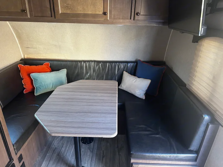 Spacious RV rental dinette interior with comfortable black seating, stylish table, and overhead cabinets for storage.. Sunset Park RV Sun Lite 2020