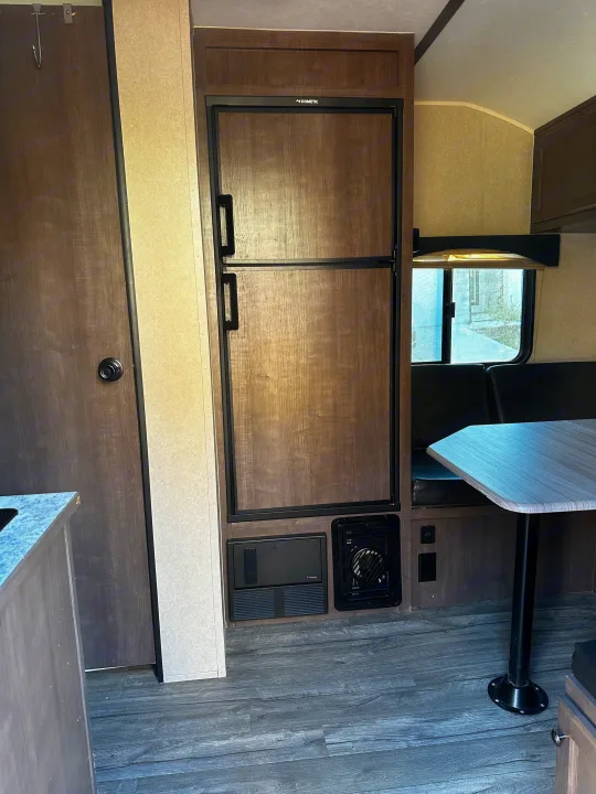 Inside an RV rental: A Dometic refrigerator, dinette seating with table, and wood-tone interior finishes.. Sunset Park RV Sun Lite 2020